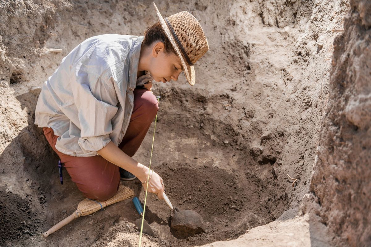 Archaeologist,Digging,With,Hand,Trowel,,Recovering,Ancient,Pottery,Object,From