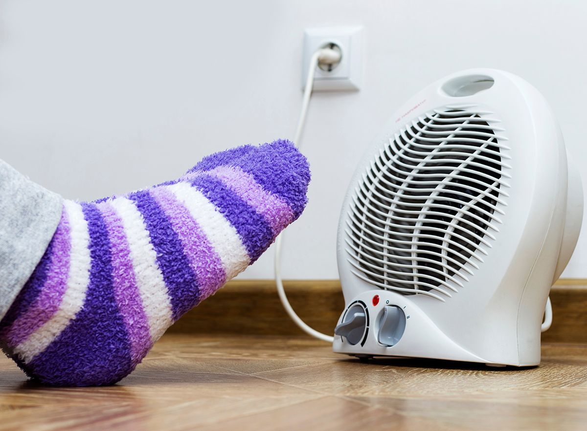 A,Woman,Warms,Her,Feet,In,Front,Of,Electric,Heater.