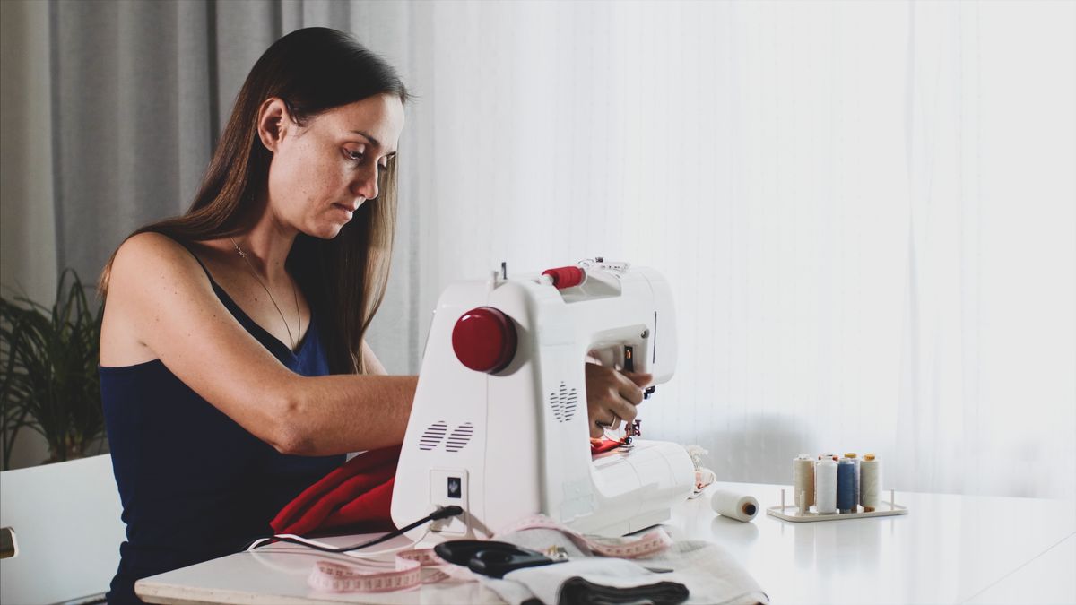 Self-employed young woman tailor working and sewing cloth on sewing machine.