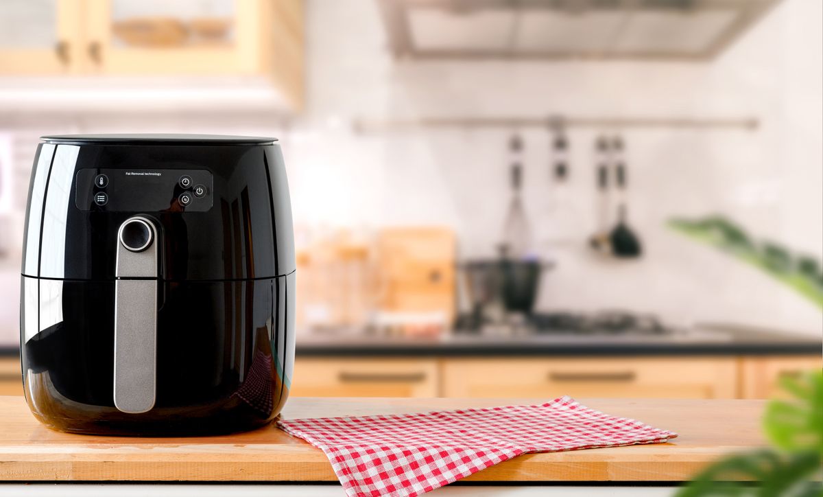 An,Electric,Air,Fryer,On,Table,With,Blurred,Kitchen,Background.