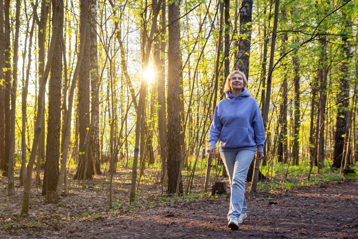 Happy woman walking in sunlit park at sunset in spring - active retirement lifestyle