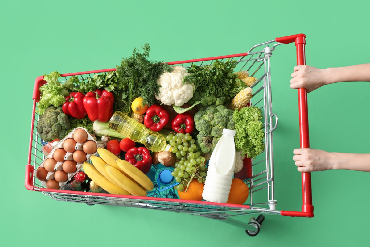 Woman,Pushing,Shopping,Cart,Full,Of,Food,On,Green,Background