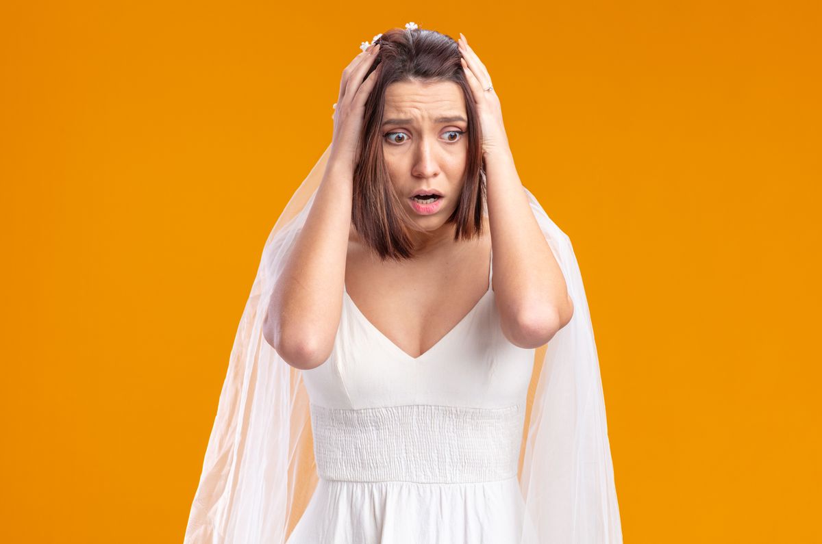 bride in beautiful wedding dress looking aside being shocked with hands on her head standing over orange background,esküvő