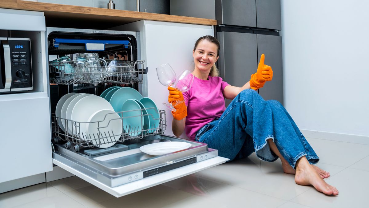 Young woman sitting on the floor near the dishwasher machine