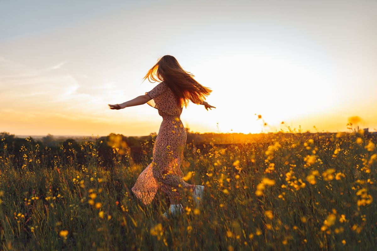 Young woman in long dress dances with joy in a rapeseed yellow field at sunset