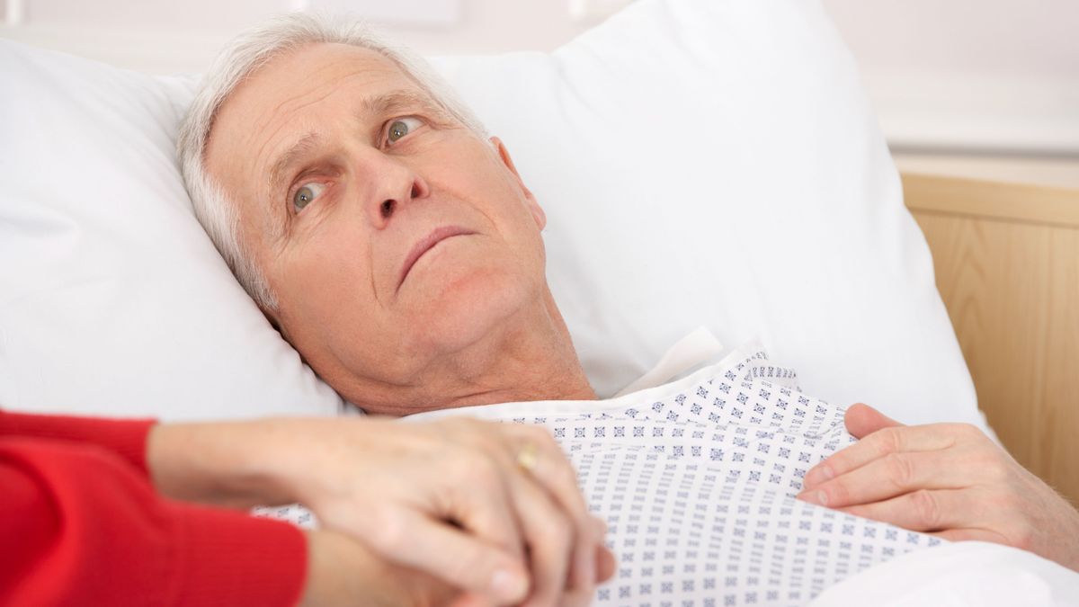 Senior man in hospital bed holding wife's hand