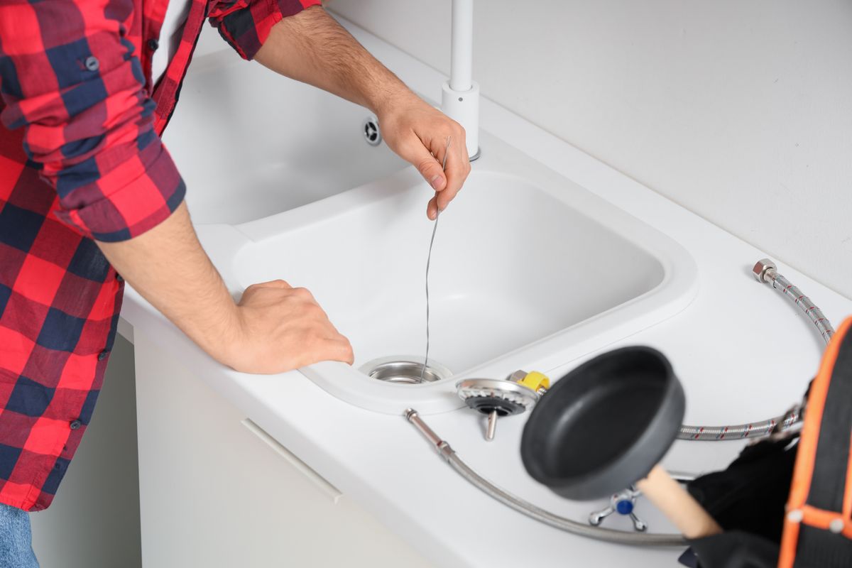 Male,Plumber,With,Wire,Clearing,Drain,In,Kitchen,,Closeup